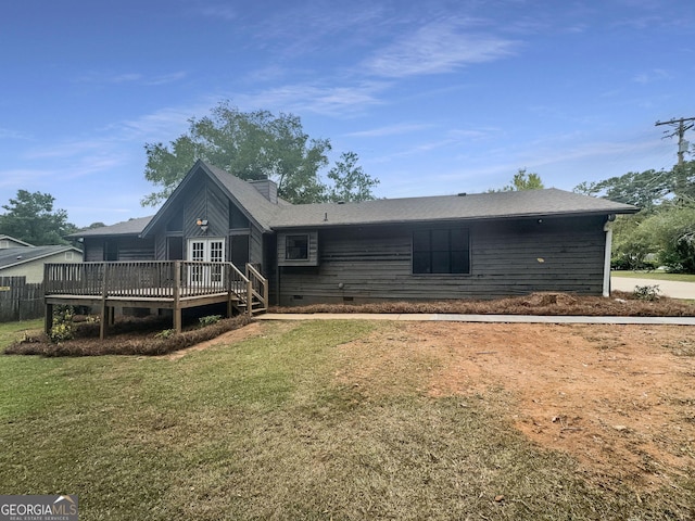 rear view of property featuring crawl space, a lawn, a deck, and roof with shingles