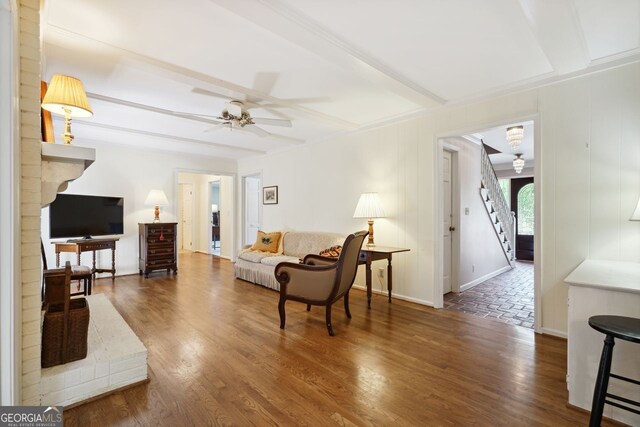 living room featuring ceiling fan, dark hardwood / wood-style floors, a brick fireplace, and beam ceiling