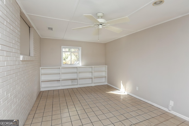 spare room featuring ceiling fan, crown molding, light tile patterned floors, and brick wall