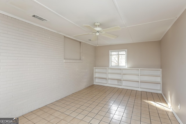 unfurnished room featuring ceiling fan, light tile patterned floors, and brick wall