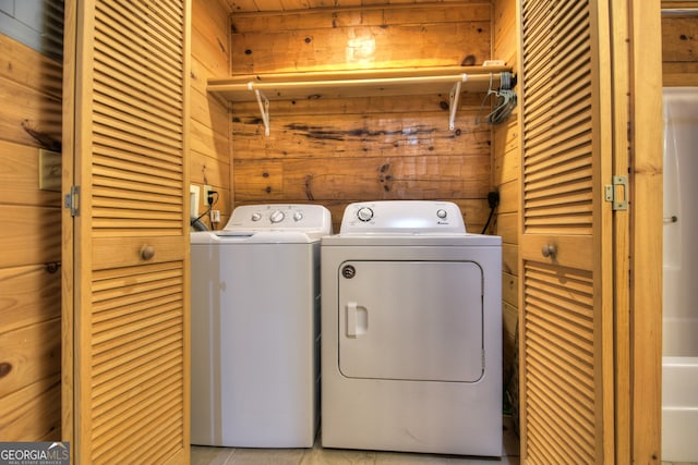 clothes washing area featuring wood walls and separate washer and dryer