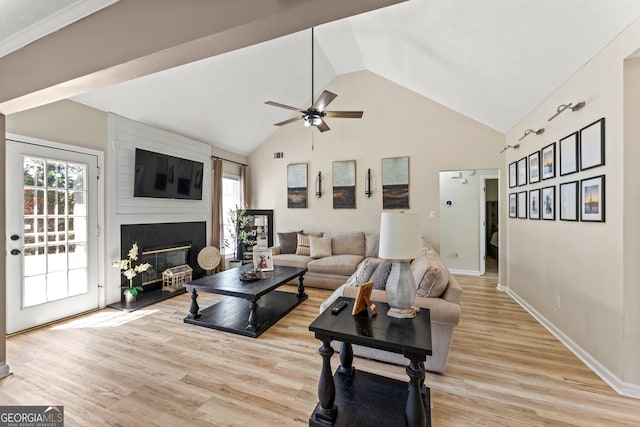 living room featuring light hardwood / wood-style floors, vaulted ceiling, ceiling fan, and a fireplace