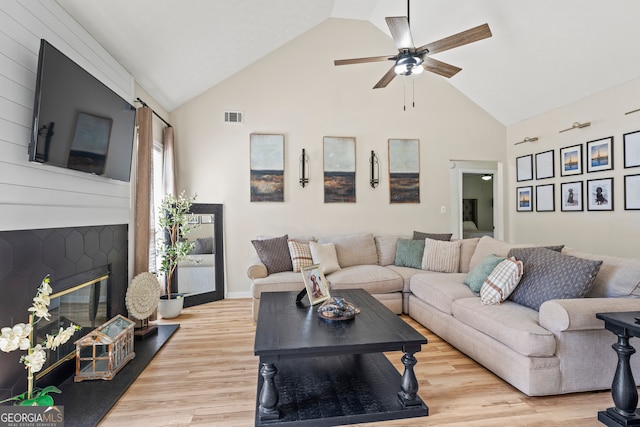 living room with light wood-type flooring, a large fireplace, ceiling fan, and high vaulted ceiling