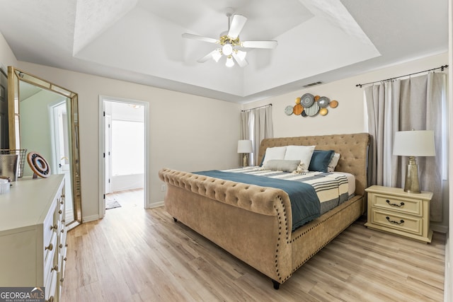 bedroom with light hardwood / wood-style flooring, ceiling fan, and a raised ceiling