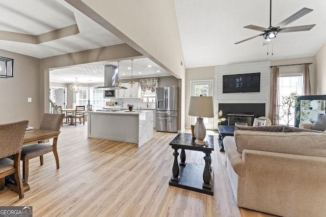 living room featuring light hardwood / wood-style floors, ceiling fan with notable chandelier, and a fireplace