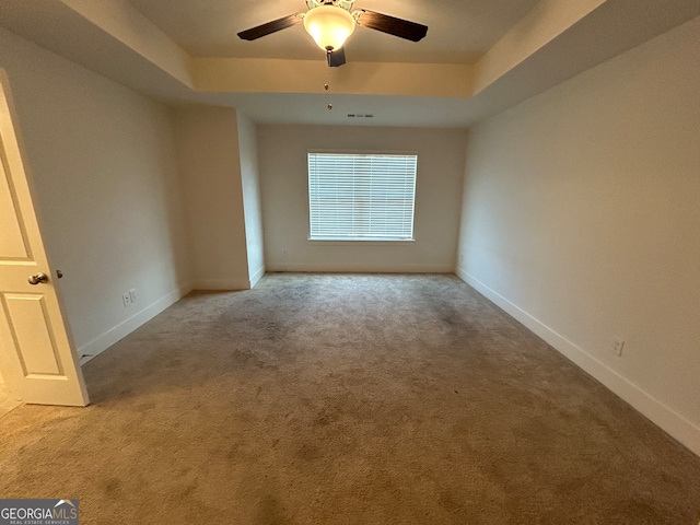 spare room with a raised ceiling, ceiling fan, and light carpet