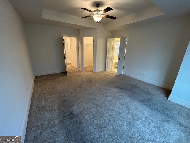 unfurnished bedroom with ceiling fan, a closet, a tray ceiling, a walk in closet, and carpet floors