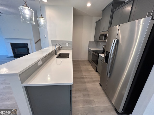 kitchen with backsplash, hanging light fixtures, appliances with stainless steel finishes, light hardwood / wood-style floors, and sink