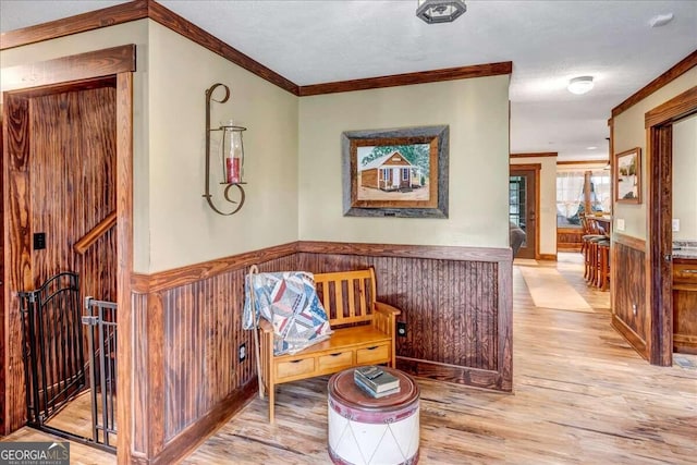 living area with ornamental molding, a textured ceiling, light hardwood / wood-style flooring, and wooden walls