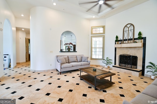 tiled living room featuring ceiling fan, a towering ceiling, and a tiled fireplace