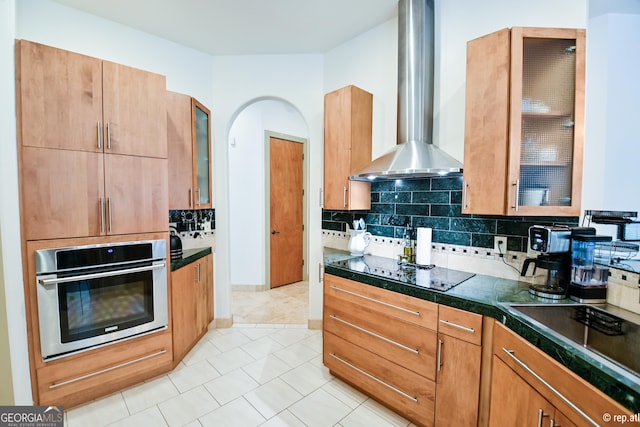 kitchen with black electric stovetop, tasteful backsplash, wall chimney range hood, light tile patterned floors, and oven