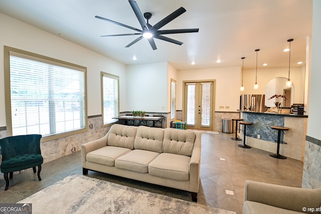 tiled living room with ceiling fan, tile walls, and french doors