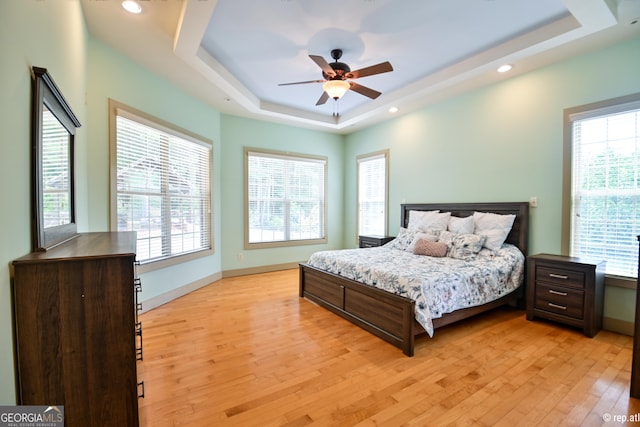 bedroom featuring light hardwood / wood-style floors, ceiling fan, and a tray ceiling