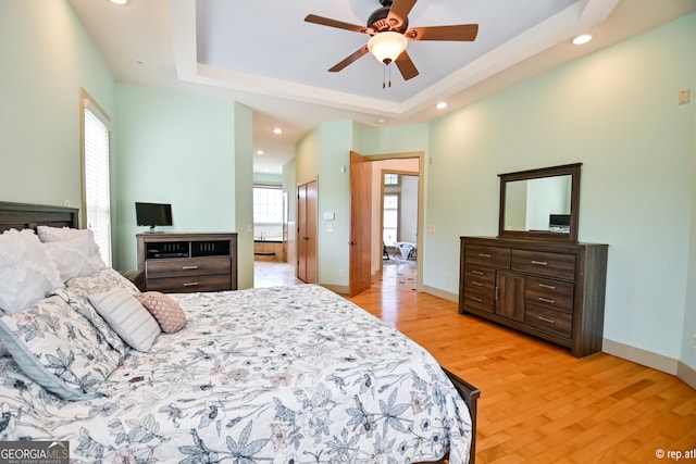 bedroom with a raised ceiling, connected bathroom, ceiling fan, and light wood-type flooring