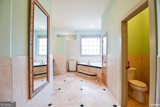 bathroom featuring tiled bath, a healthy amount of sunlight, tile walls, and toilet