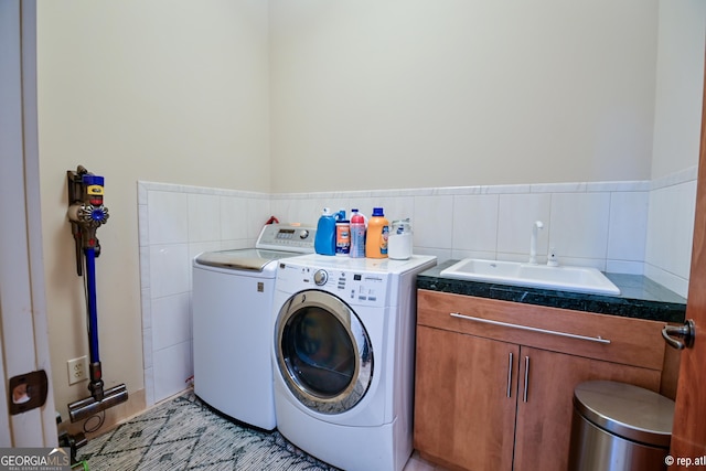 laundry area with washing machine and clothes dryer, sink, cabinets, and tile walls