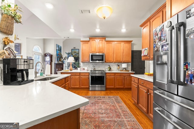 kitchen with tasteful backsplash, appliances with stainless steel finishes, sink, light hardwood / wood-style floors, and a kitchen island with sink