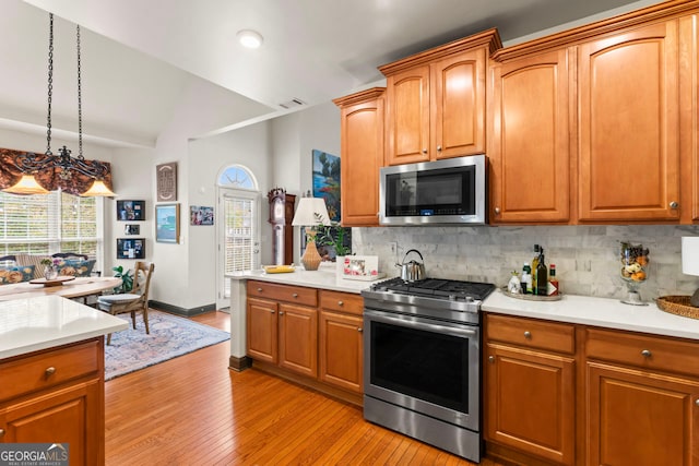 kitchen featuring vaulted ceiling, tasteful backsplash, pendant lighting, light wood-type flooring, and appliances with stainless steel finishes