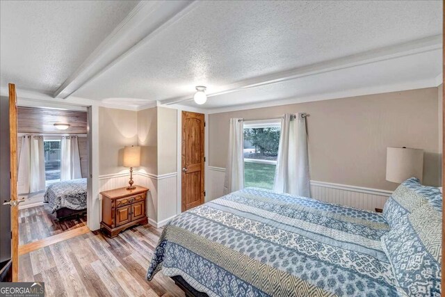 bedroom with a textured ceiling, beamed ceiling, and hardwood / wood-style floors