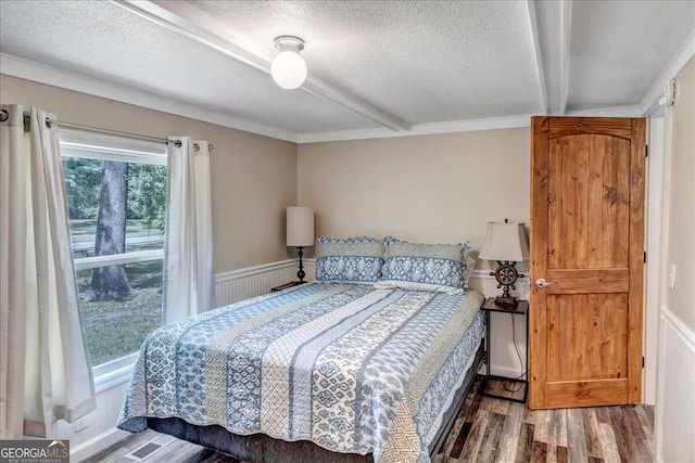 bedroom with hardwood / wood-style floors, beamed ceiling, and a textured ceiling