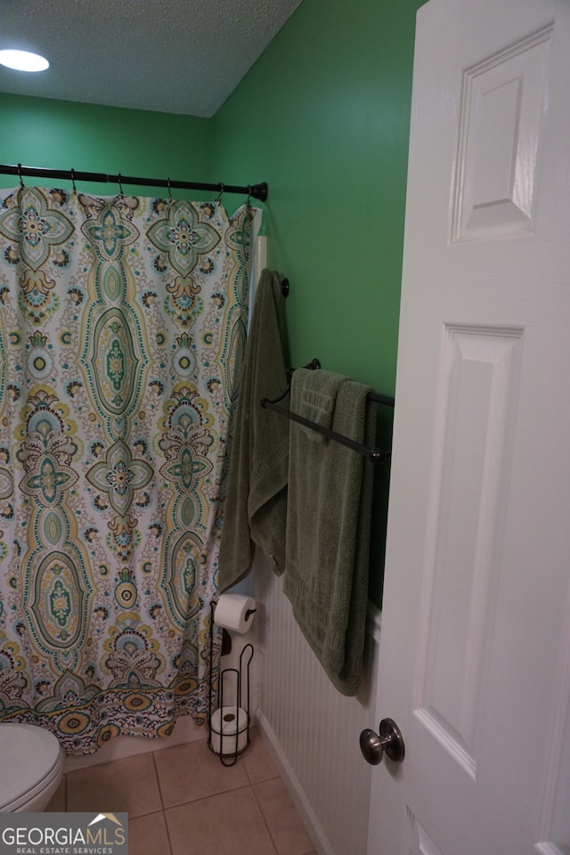 bathroom featuring toilet, a shower with curtain, tile patterned floors, and a textured ceiling