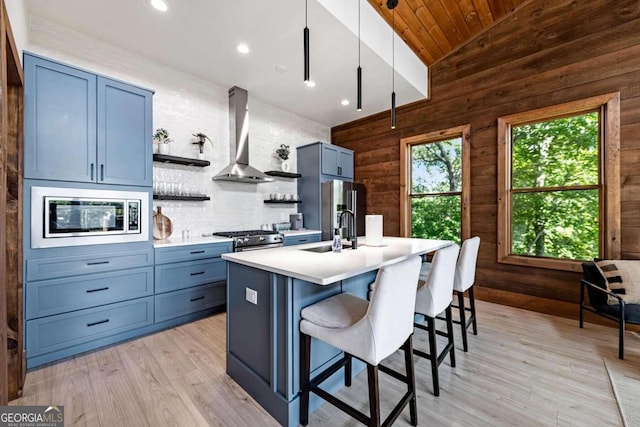 kitchen featuring vaulted ceiling, a center island with sink, appliances with stainless steel finishes, a breakfast bar, and wall chimney range hood