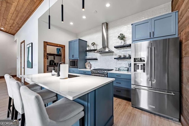 kitchen with blue cabinetry, premium appliances, wall chimney exhaust hood, a kitchen breakfast bar, and a center island with sink