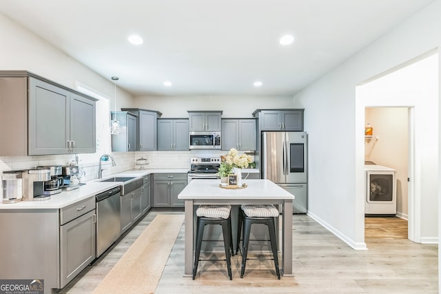 kitchen featuring light hardwood / wood-style flooring, stainless steel appliances, a center island, a breakfast bar area, and washer / clothes dryer