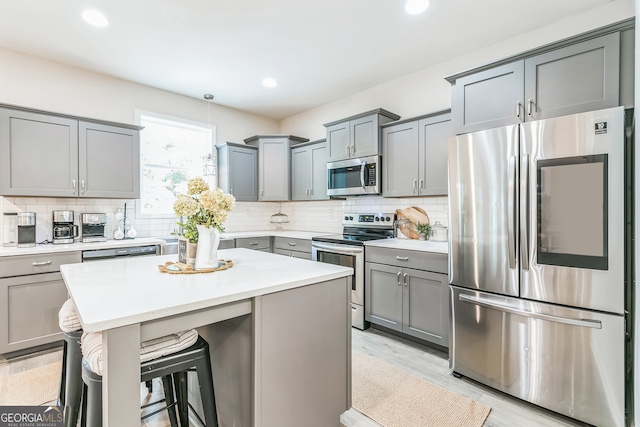 kitchen with appliances with stainless steel finishes, light hardwood / wood-style floors, a kitchen island, decorative backsplash, and a breakfast bar