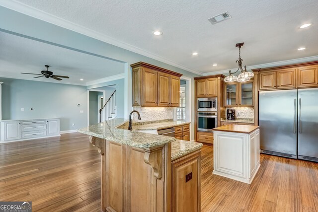 kitchen with ceiling fan with notable chandelier, built in appliances, light hardwood / wood-style flooring, light stone counters, and hanging light fixtures