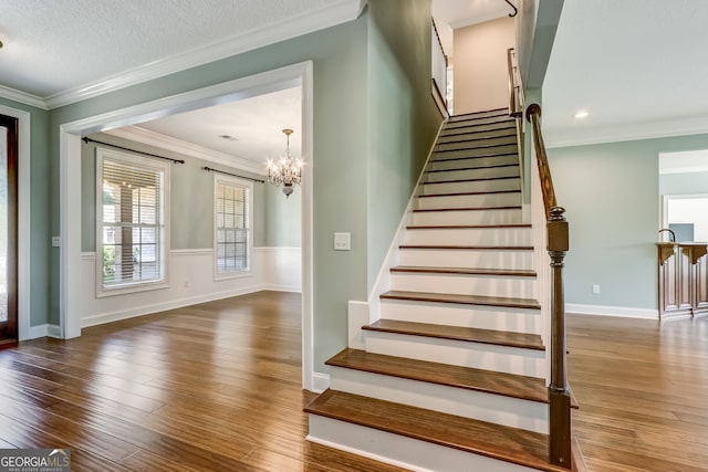 stairway featuring ornamental molding, an inviting chandelier, wood-type flooring, and a textured ceiling