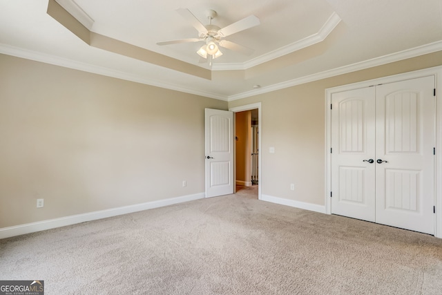 unfurnished bedroom with light carpet, ornamental molding, ceiling fan, a closet, and a raised ceiling