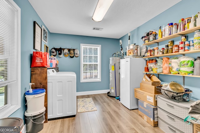 laundry area with plenty of natural light, light hardwood / wood-style floors, a textured ceiling, and electric water heater