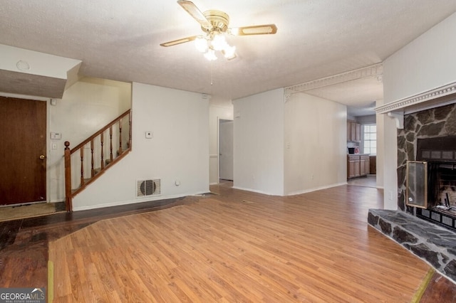 living room featuring a fireplace, a textured ceiling, wood-type flooring, and ceiling fan