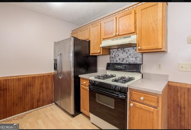 kitchen featuring wooden walls, a textured ceiling, light hardwood / wood-style flooring, gas range gas stove, and stainless steel fridge with ice dispenser