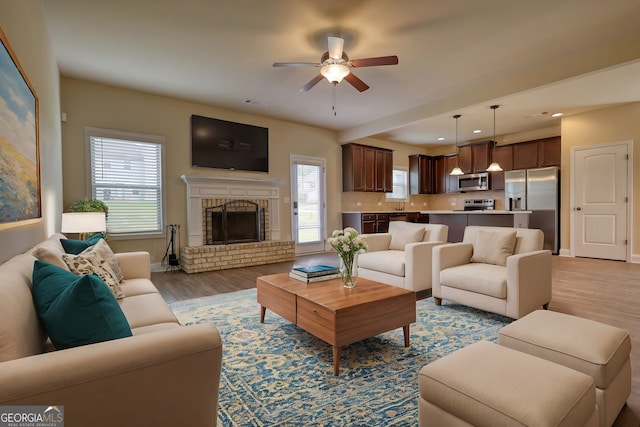 living room featuring a fireplace, wood-type flooring, sink, and ceiling fan