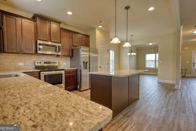 kitchen with light stone countertops, appliances with stainless steel finishes, tasteful backsplash, light hardwood / wood-style floors, and a center island