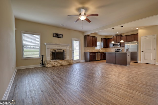 unfurnished living room with a brick fireplace, sink, ceiling fan, and light hardwood / wood-style floors