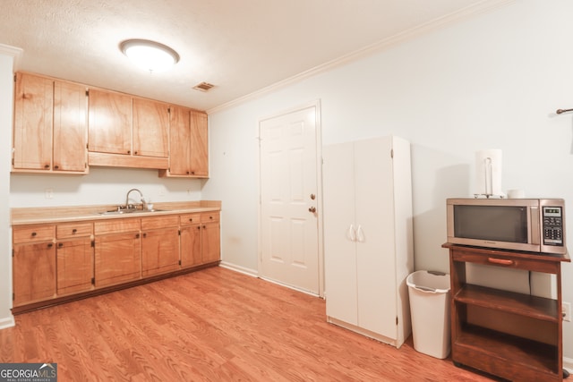 kitchen with a textured ceiling, light brown cabinetry, light hardwood / wood-style floors, ornamental molding, and sink