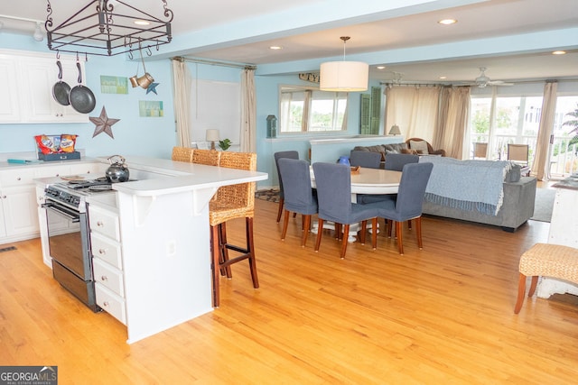 kitchen with white cabinets, a kitchen island, pendant lighting, light wood-type flooring, and black gas stove