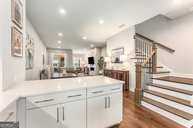 kitchen featuring light stone counters, dark wood-type flooring, kitchen peninsula, and white cabinetry