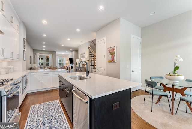 kitchen with dark wood-type flooring, a kitchen island with sink, sink, white cabinets, and appliances with stainless steel finishes