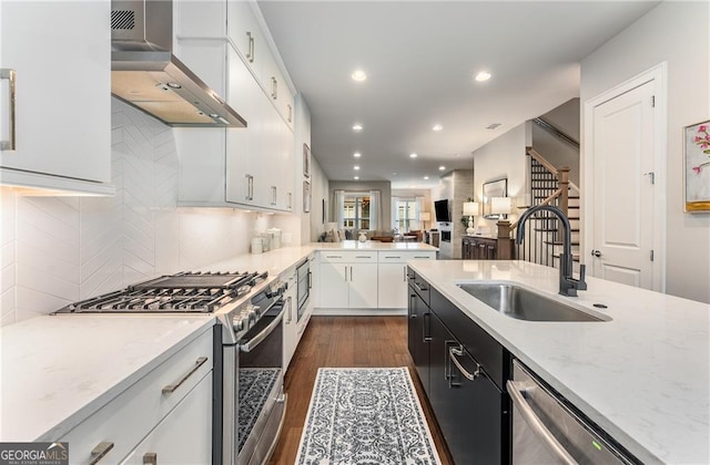 kitchen with dark wood-type flooring, sink, white cabinets, wall chimney exhaust hood, and stainless steel appliances