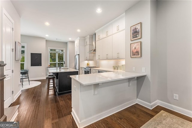 kitchen featuring white cabinets, kitchen peninsula, wall chimney exhaust hood, dark hardwood / wood-style floors, and a breakfast bar area