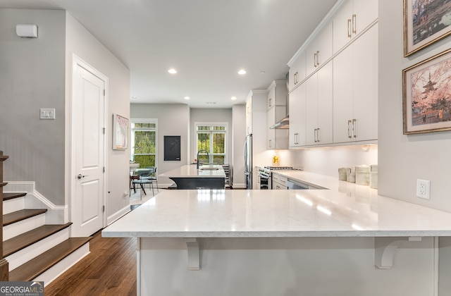 kitchen featuring kitchen peninsula, light stone countertops, a breakfast bar area, stainless steel appliances, and dark hardwood / wood-style floors