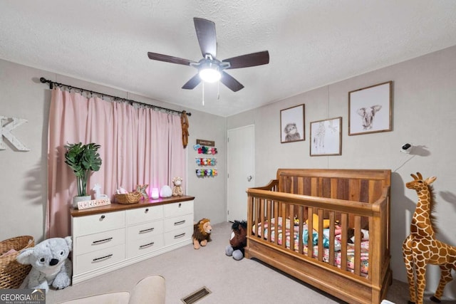 carpeted bedroom with a textured ceiling, a nursery area, and ceiling fan