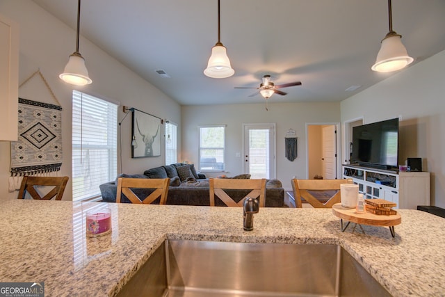 kitchen with ceiling fan, light stone counters, pendant lighting, and sink