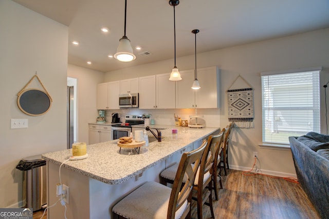 kitchen featuring decorative light fixtures, dark hardwood / wood-style flooring, kitchen peninsula, appliances with stainless steel finishes, and white cabinets