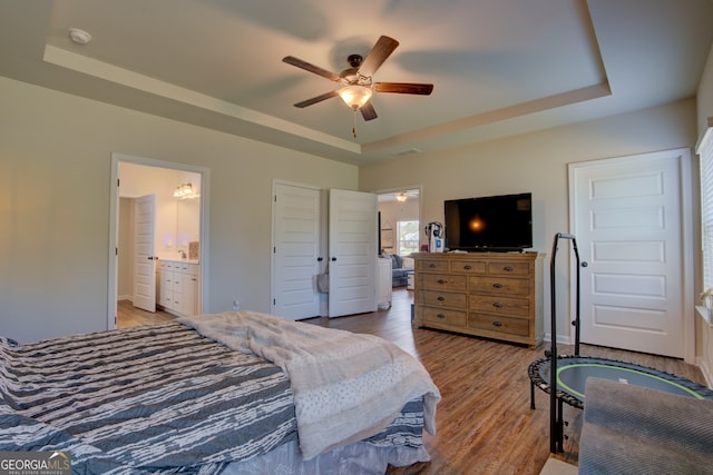 bedroom featuring ceiling fan, ensuite bathroom, a raised ceiling, and light hardwood / wood-style flooring