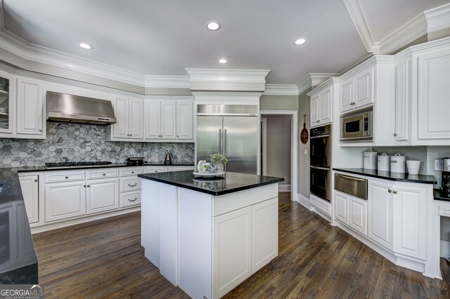 kitchen with built in appliances, dark hardwood / wood-style flooring, wall chimney exhaust hood, and white cabinets